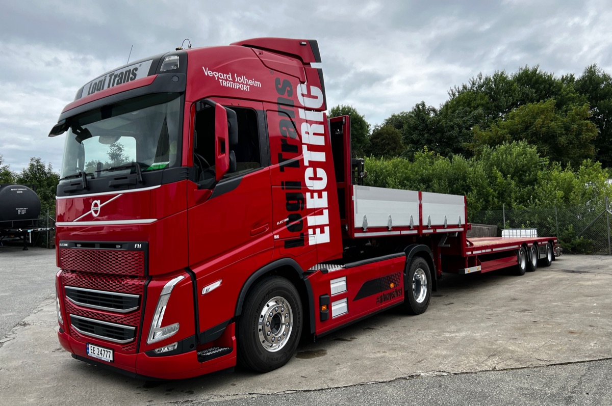 A red Logi Trans electric Volvo truck and flatbed trailer parked on tarmac.